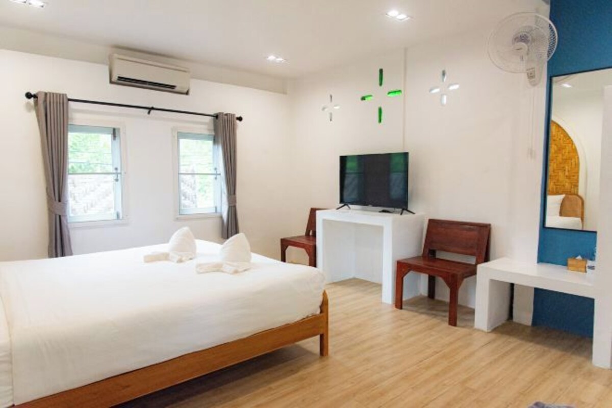 A hotel room with a bed, a desk, a chair, a TV, and a fan.