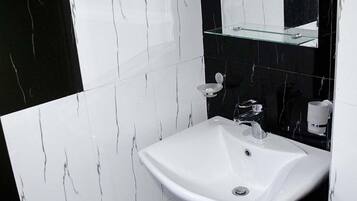 Une salle de bain avec un lavabo blanc, des murs carrelés en noir et blanc, et une étagère en verre au-dessus du lavabo.
