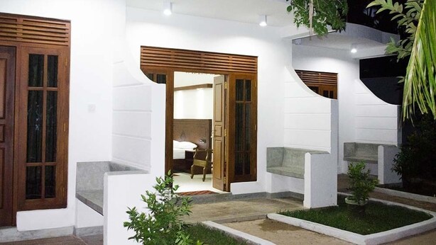 Un bâtiment moderne aux murs blancs et aux éléments décoratifs en bois, doté d’une entrée bien éclairée et d’un petit espace jardin.