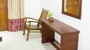 Une pièce avec un bureau en bois, une chaise, un miroir et une fenêtre avec des rideaux.