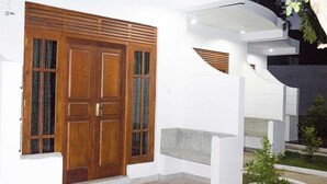 Un bâtiment moderne doté d’une grande porte en bois, de murs blancs et d’un petit espace jardin.