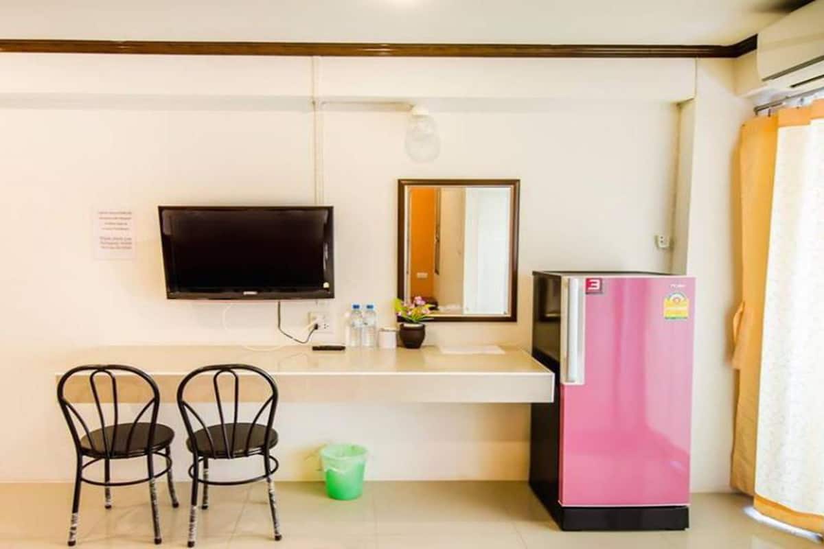 Eine kleine Küchenzeile mit einem rosa Kühlschrank, einem Flachbildfernseher an der Wand, einem Spiegel und zwei Stühlen.