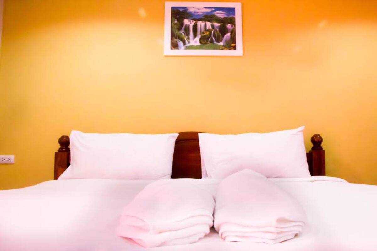 Ein Bett mit weißer Bettwäsche und Kissen, ein hölzerner Kopfteil und ein gerahmtes Bild eines Wasserfalls an der Wand.