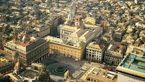 Vista aérea de una ciudad histórica con una plaza destacada, edificios circundantes y un puerto con barcos.