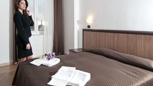 Una habitación de hotel con una cama grande, una mesita de noche, una ventana con cortinas y vistas a la ciudad.
