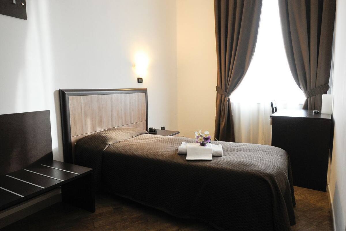 A hotel room with a bed, bedside table, and a small desk with a lamp.