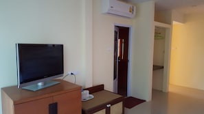 Un televisor sobre un mueble de madera, un enchufe y una puerta que da a otra habitación.
