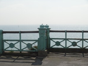 A turquoise metal railing with a clock, overlooking a body of water. - Brighton Break - Burlington Beach Pad (Brighton)