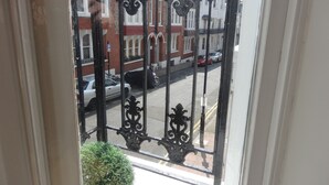 A view through a black wrought iron gate with a white door frame, leading to a street with parked cars and a red car in the distance. - Brighton Break - Burlington Beach Pad (Brighton)