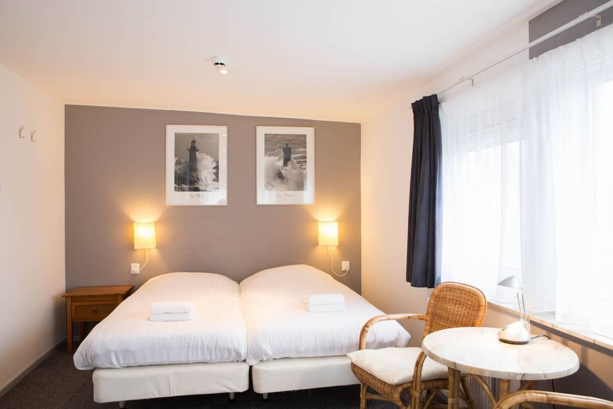 A hotel room with two beds, a small table, a chair, and two wall-mounted lights.