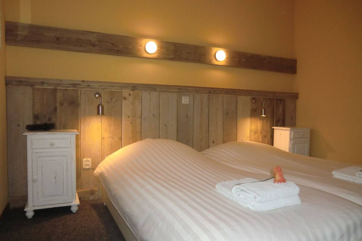 A hotel room with two beds, wooden headboard, bedside lamps, a small white cabinet, and a white dresser.