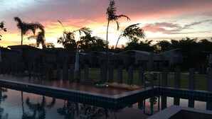 A swimming pool with a sunset view, surrounded by palm trees and modern buildings. - Baanwaan Resort Hat Yai (Hat Yai)