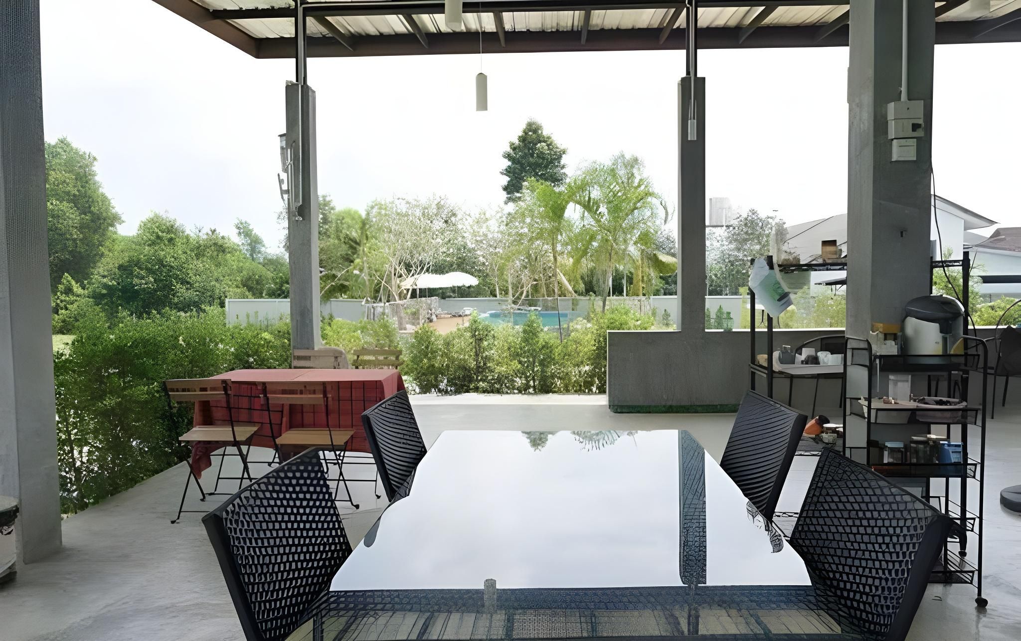 Une terrasse extérieure avec une table et des chaises en verre, une piscine en arrière-plan et une vue sur la verdure et les bâtiments.