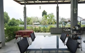 An outdoor patio with a glass table and chairs, a pool in the background, and a view of greenery and buildings. - Baanwaan Resort Hat Yai (Hat Yai)