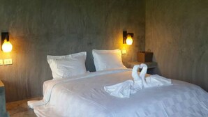 A neatly made bed with a swan-shaped pillow arrangement, two wall-mounted lamps, and a wooden nightstand with a bag. - Baanwaan Resort Hat Yai (Hat Yai)