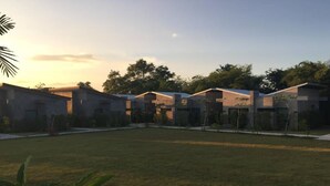 A row of modern, single-story buildings with flat roofs, arranged in a linear fashion along a grassy area with trees in the background. - Baanwaan Resort Hat Yai (Hat Yai)