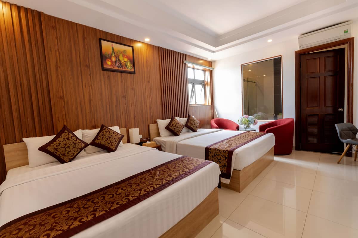 A hotel room with two beds, wooden paneling on the walls, a large mirror, and a red chair.