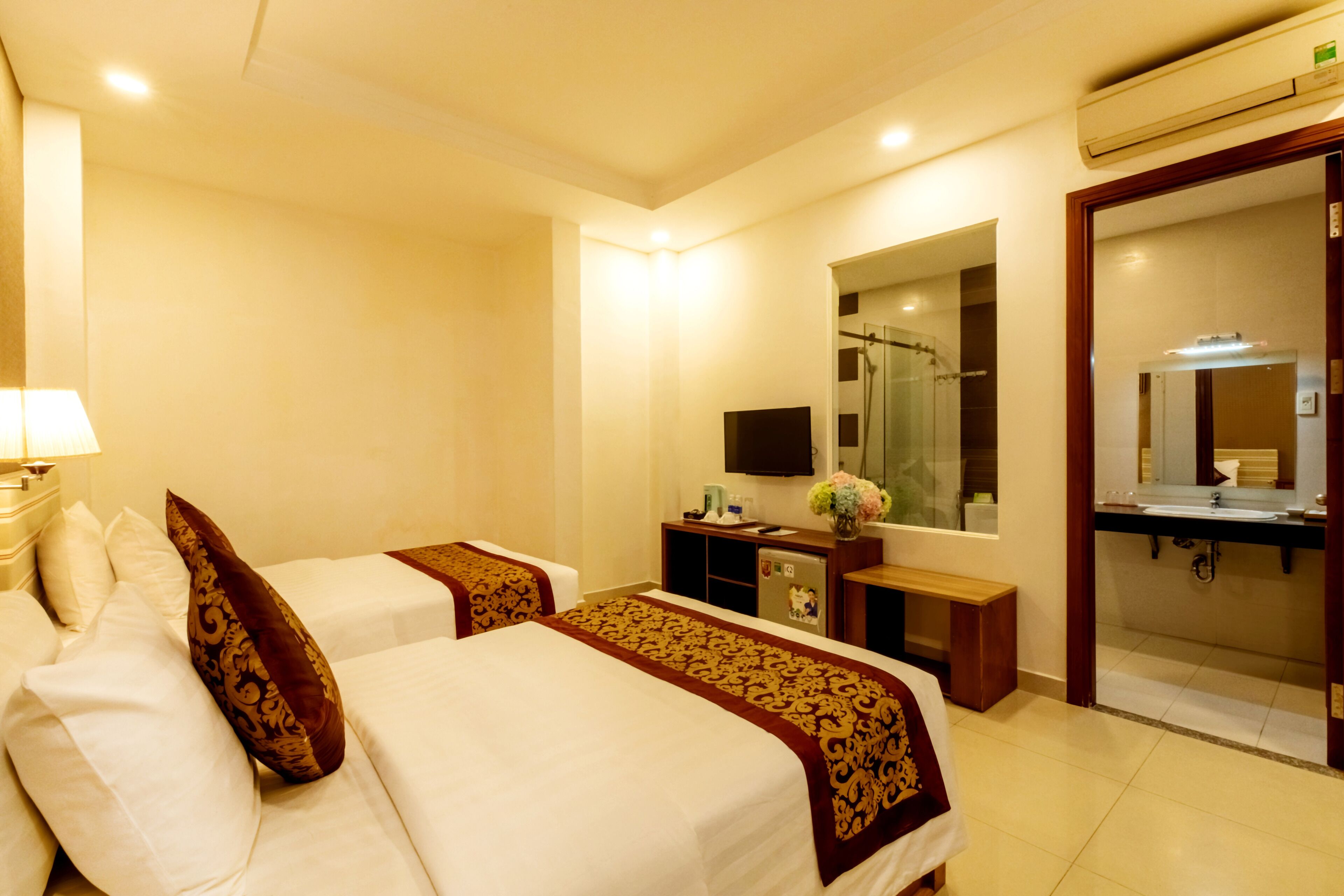 Habitación de hotel con dos camas, un escritorio con computadora, un espejo y baño con lavamanos y ducha.