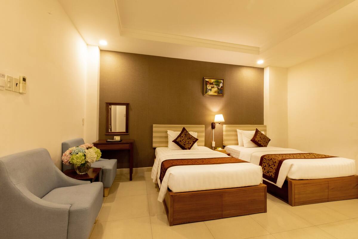A hotel room with two beds, a sofa, a nightstand, and a wall-mounted mirror.