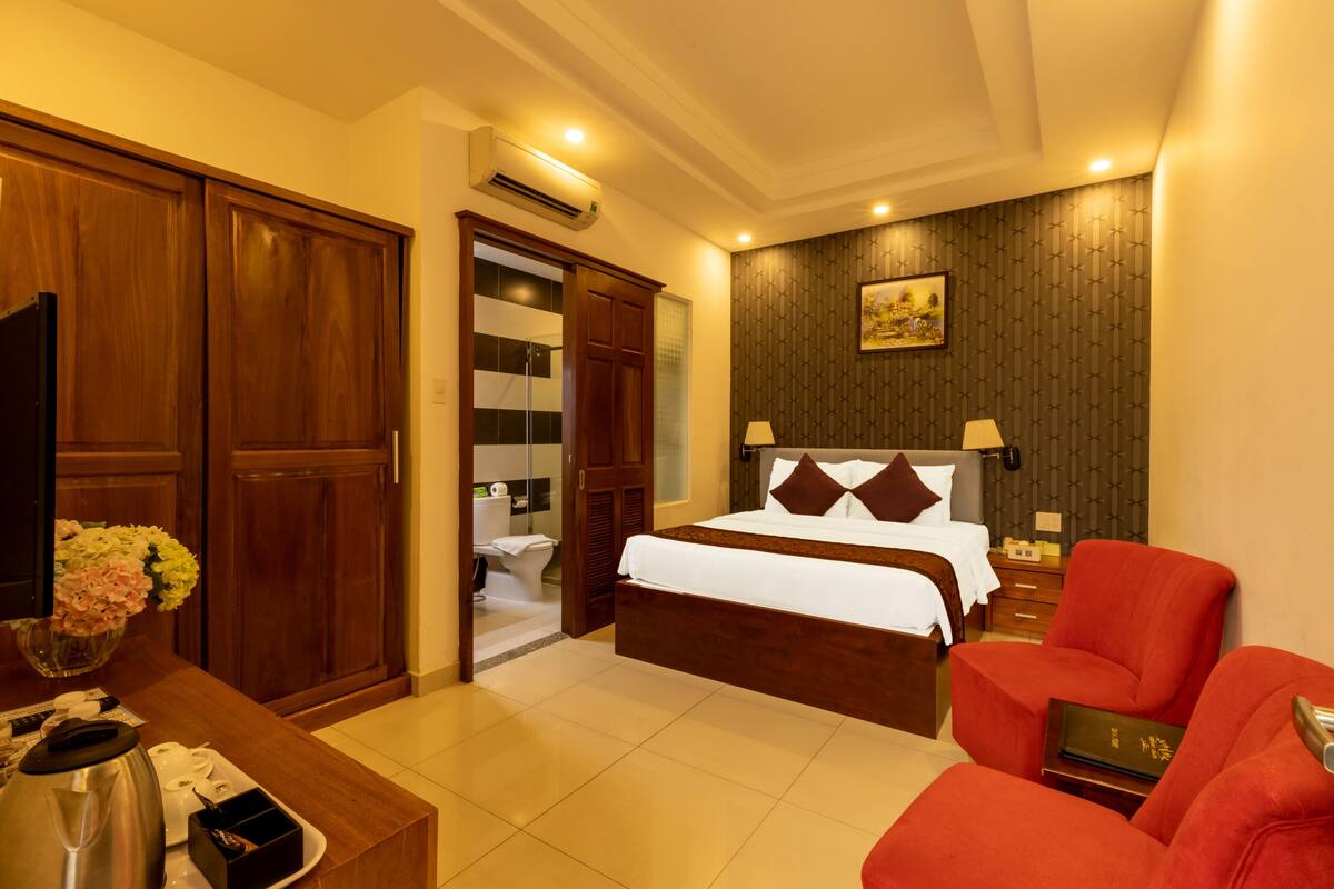 A hotel room with a bed, a desk with a coffee maker, a red armchair, and a TV.