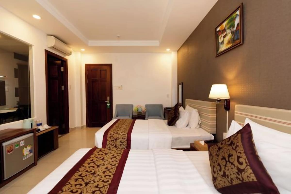 A hotel room with two beds, a desk, a chair, a lamp, and a painting on the wall.