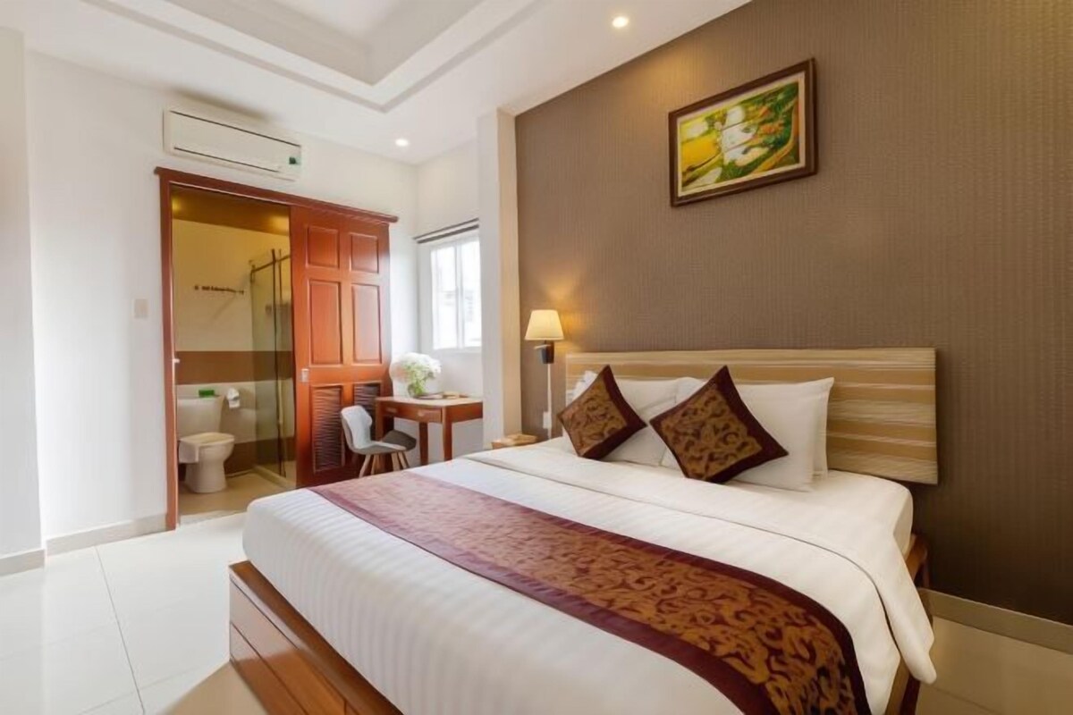 Habitación de hotel con una cama grande, un escritorio, una silla y un baño con puerta de vidrio.