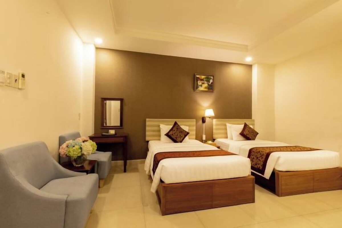 Habitación de hotel con dos camas, un sofá, una mesita de noche y un espejo.