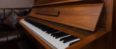 Un piano de cola en una habitación con un sofá de cuero oscuro y un jarrón de flores rosas.