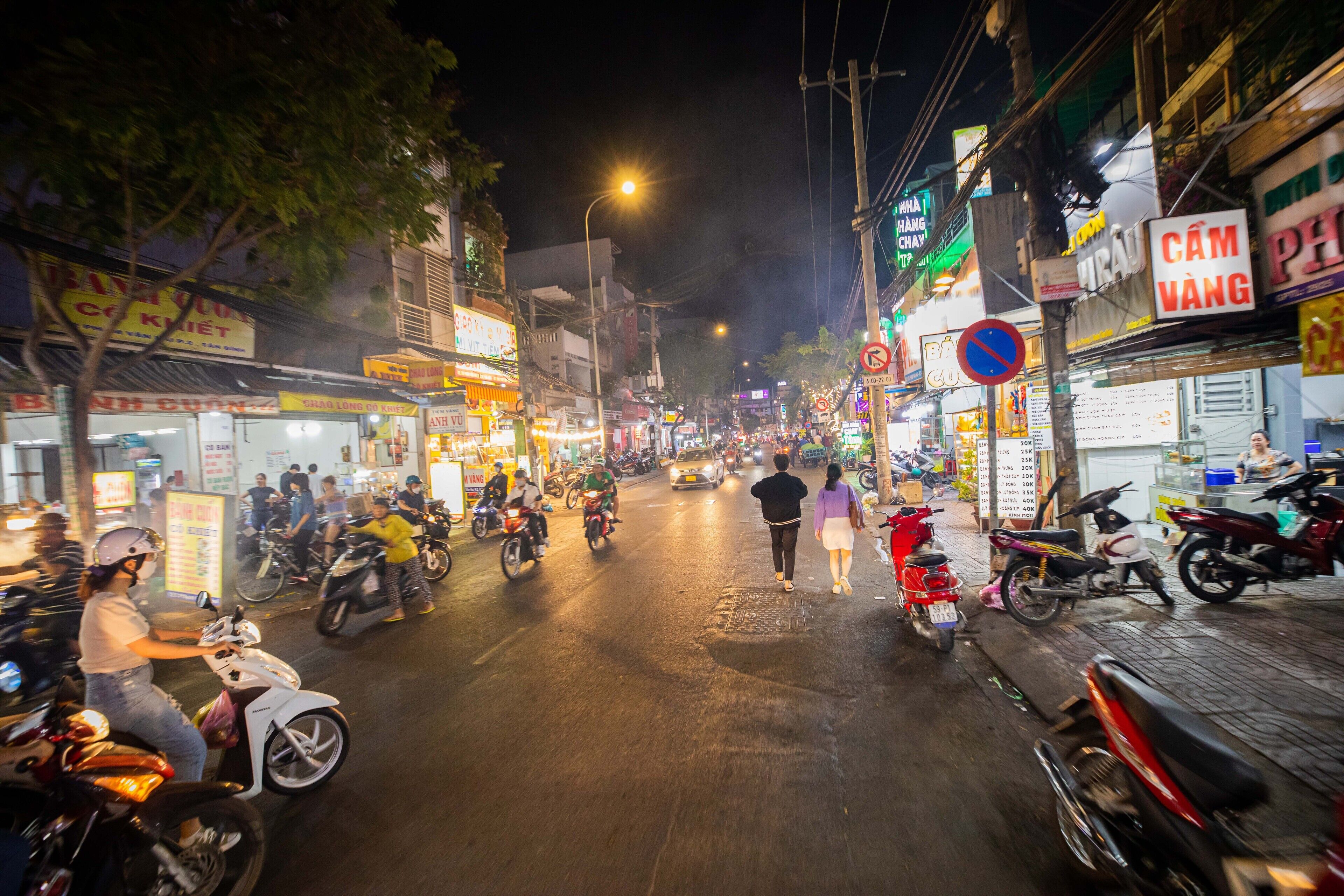 Een levendige straat 's nachts met verschillende winkels en scooters.