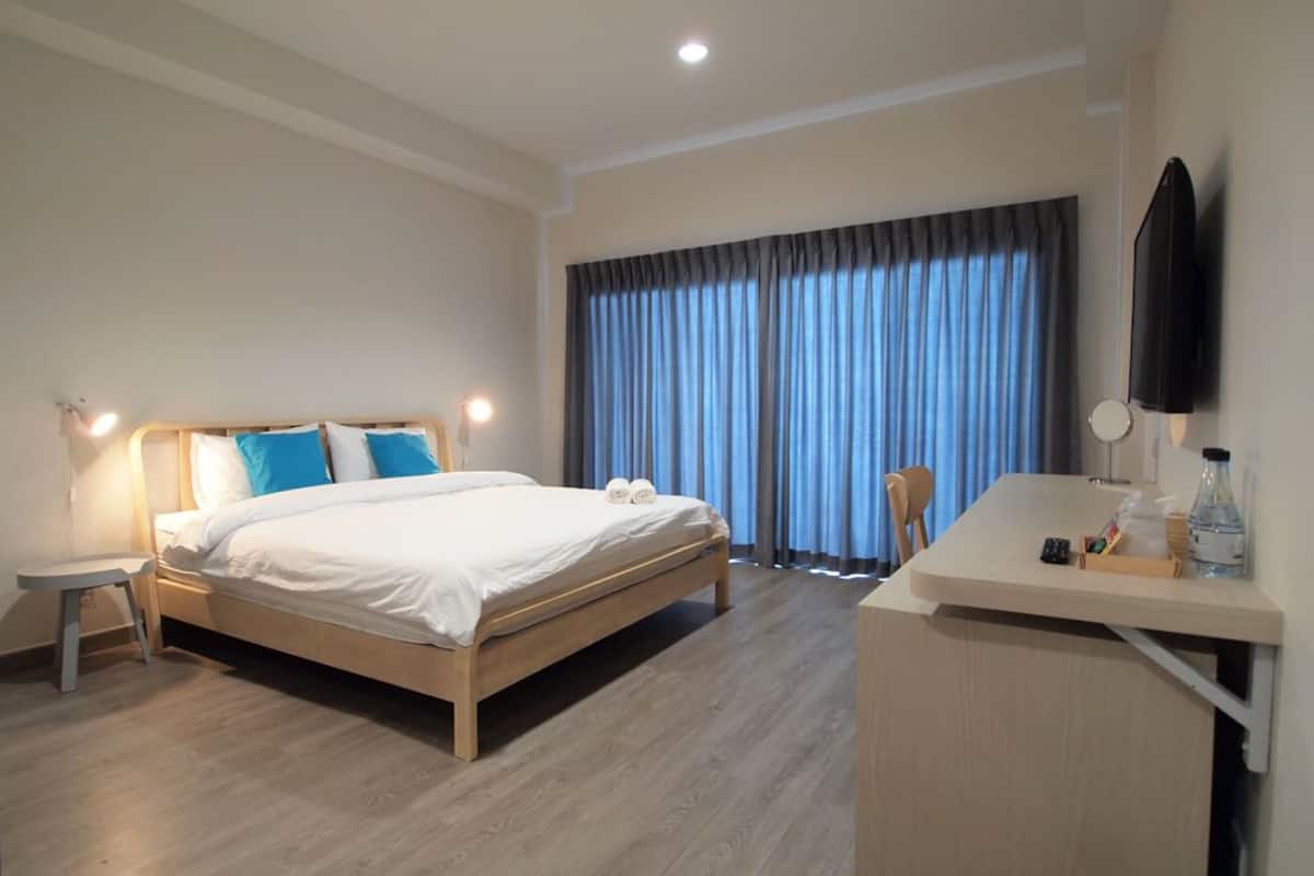Ein Hotelzimmer mit Bett, Nachttisch, Schreibtisch, Stuhl und einem an der Wand montierten Fernseher.
