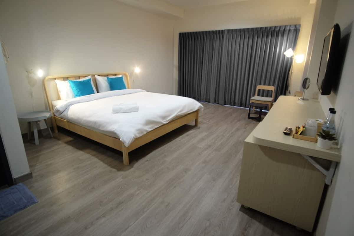 Ein Hotelzimmer mit einem hölzernen Bett, einem Schreibtisch mit Lampe und einem großen Fenster mit Vorhängen.