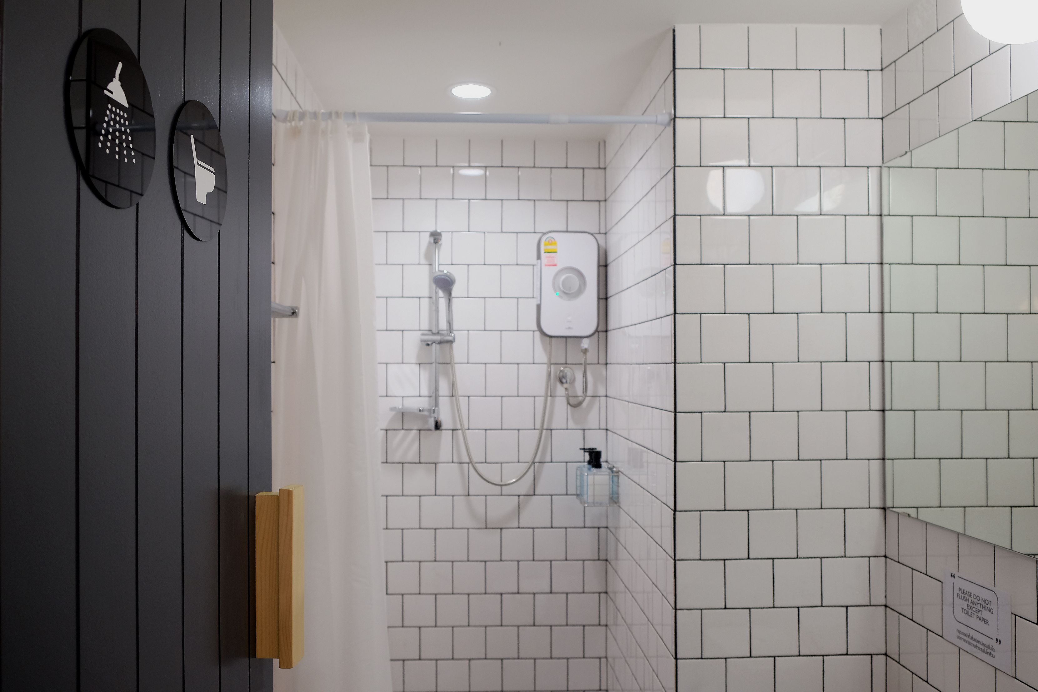 A bathroom with white tiled walls, a shower, and a toilet.