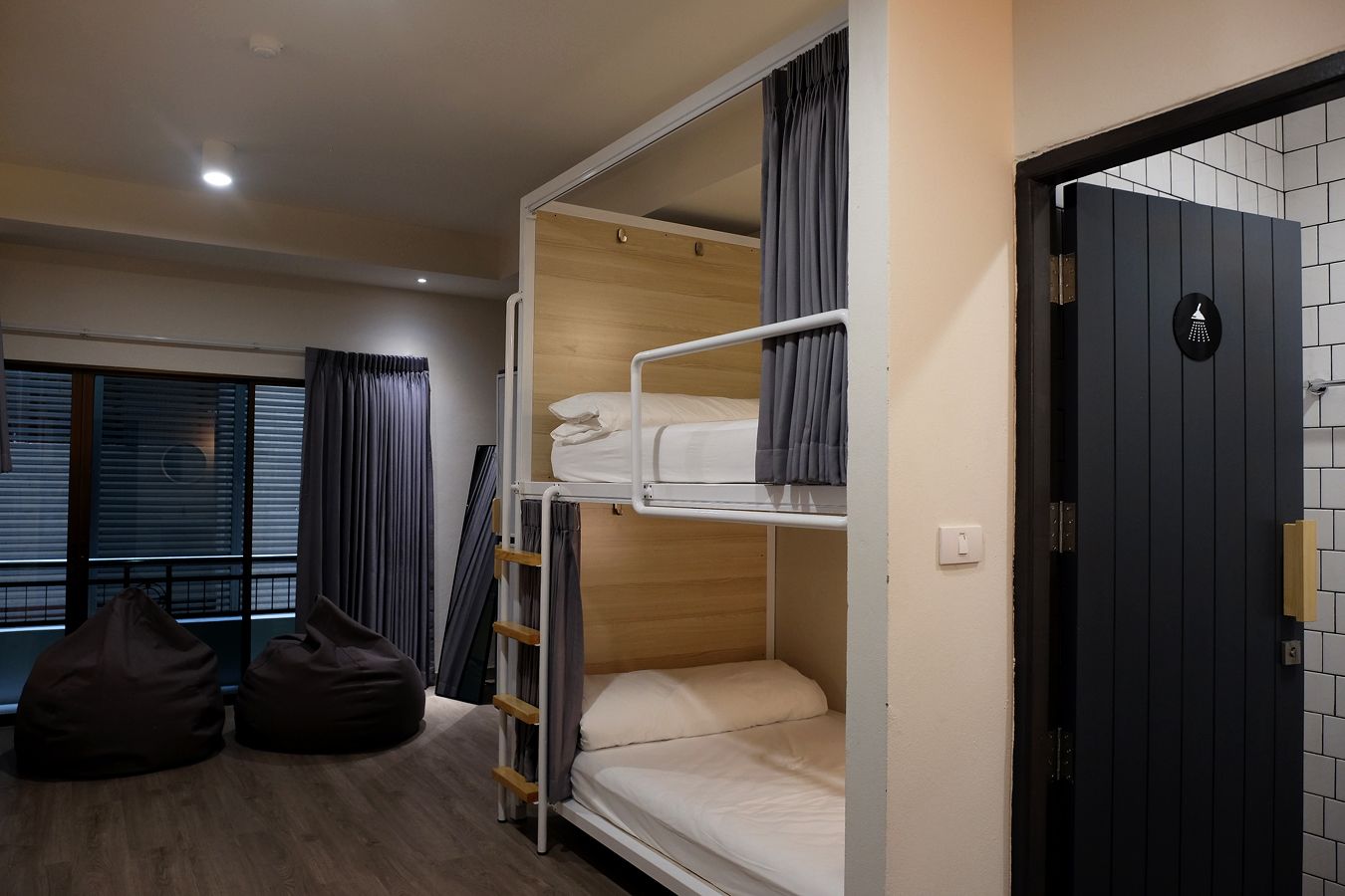 A bunk bed room with a ladder, a window with curtains, and a door with a towel rack.