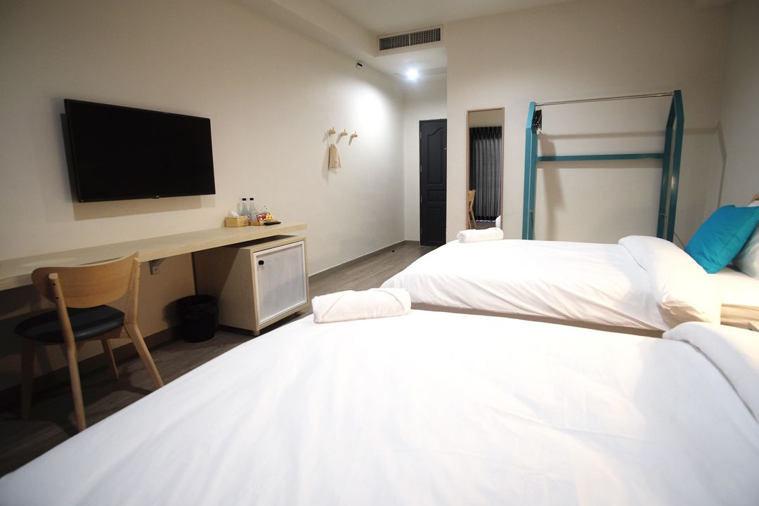 A hotel room with two beds, a desk, a chair, a TV, and a bunk bed.