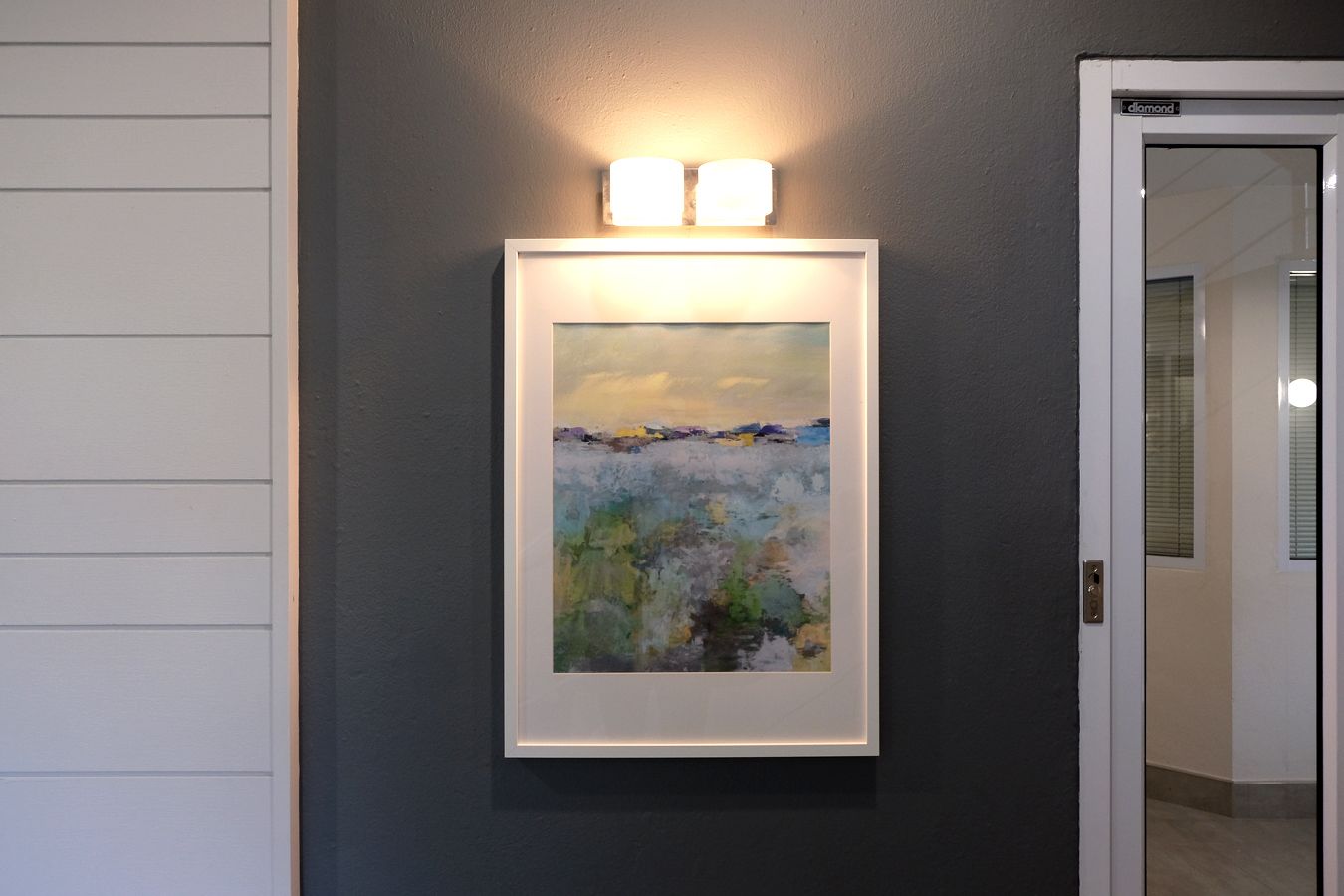 A framed painting on a wall with a door to the right.
