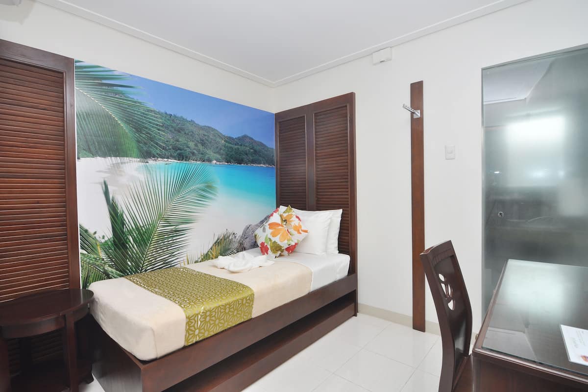 A bedroom with a bed, wooden shutters, a glass table, and a mural of a beach scene.