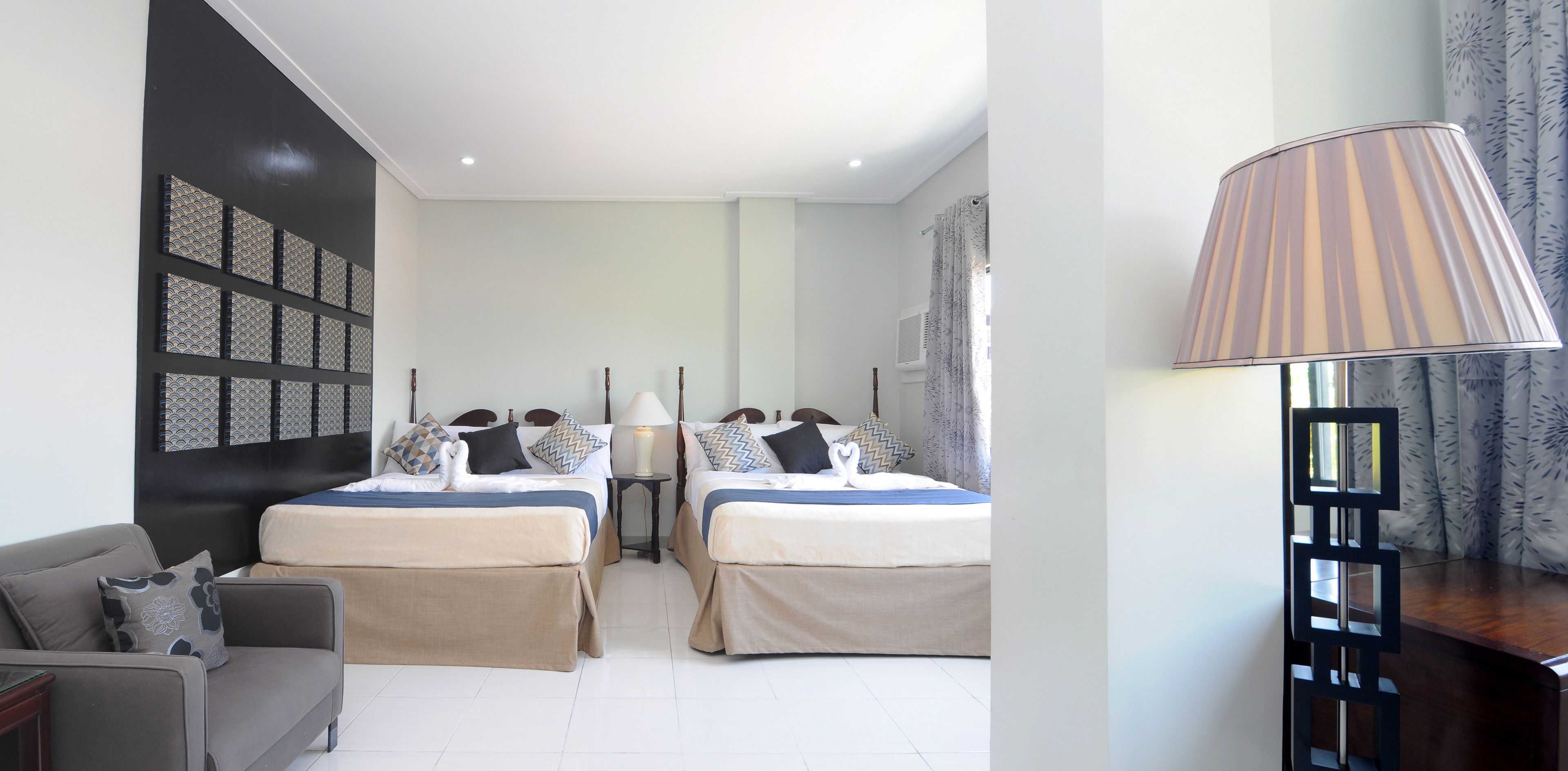 A hotel room with two beds, a sofa, a lamp, and a decorative wall panel.