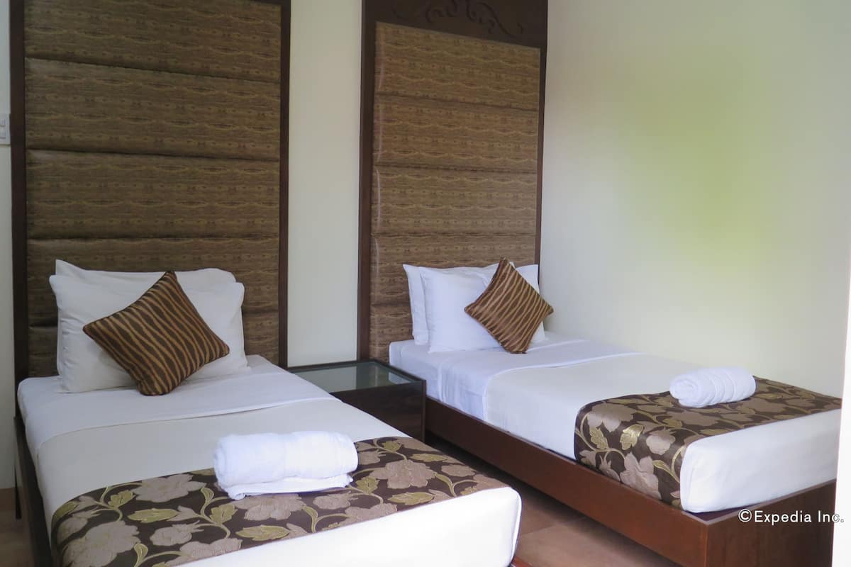 Two single beds with wooden headboards, white linens, and brown patterned pillows.