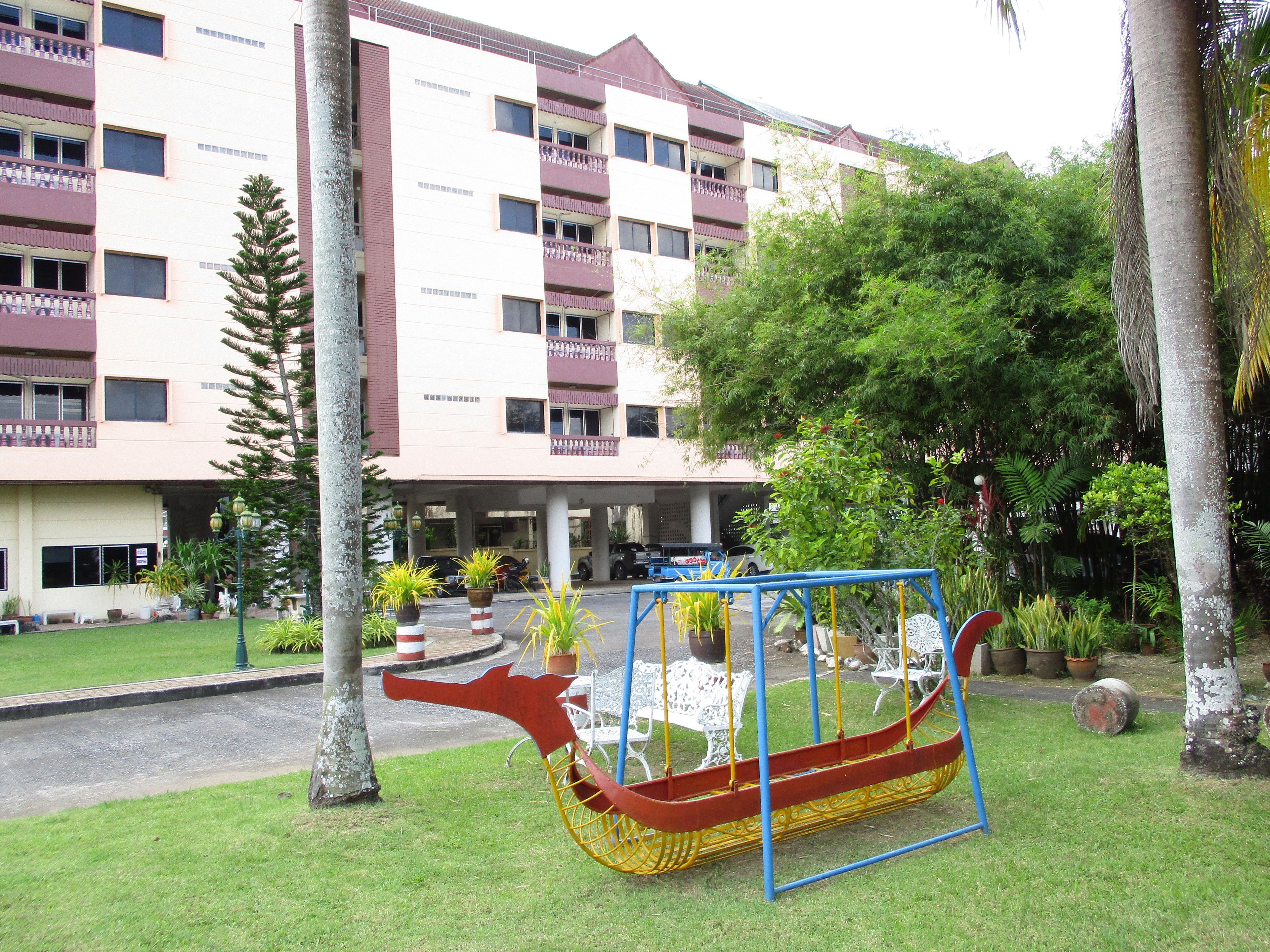A building with multiple balconies and a garden area with a swing set.