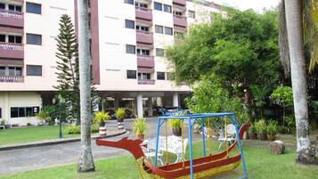 A building with multiple balconies and a garden area with a swing set.