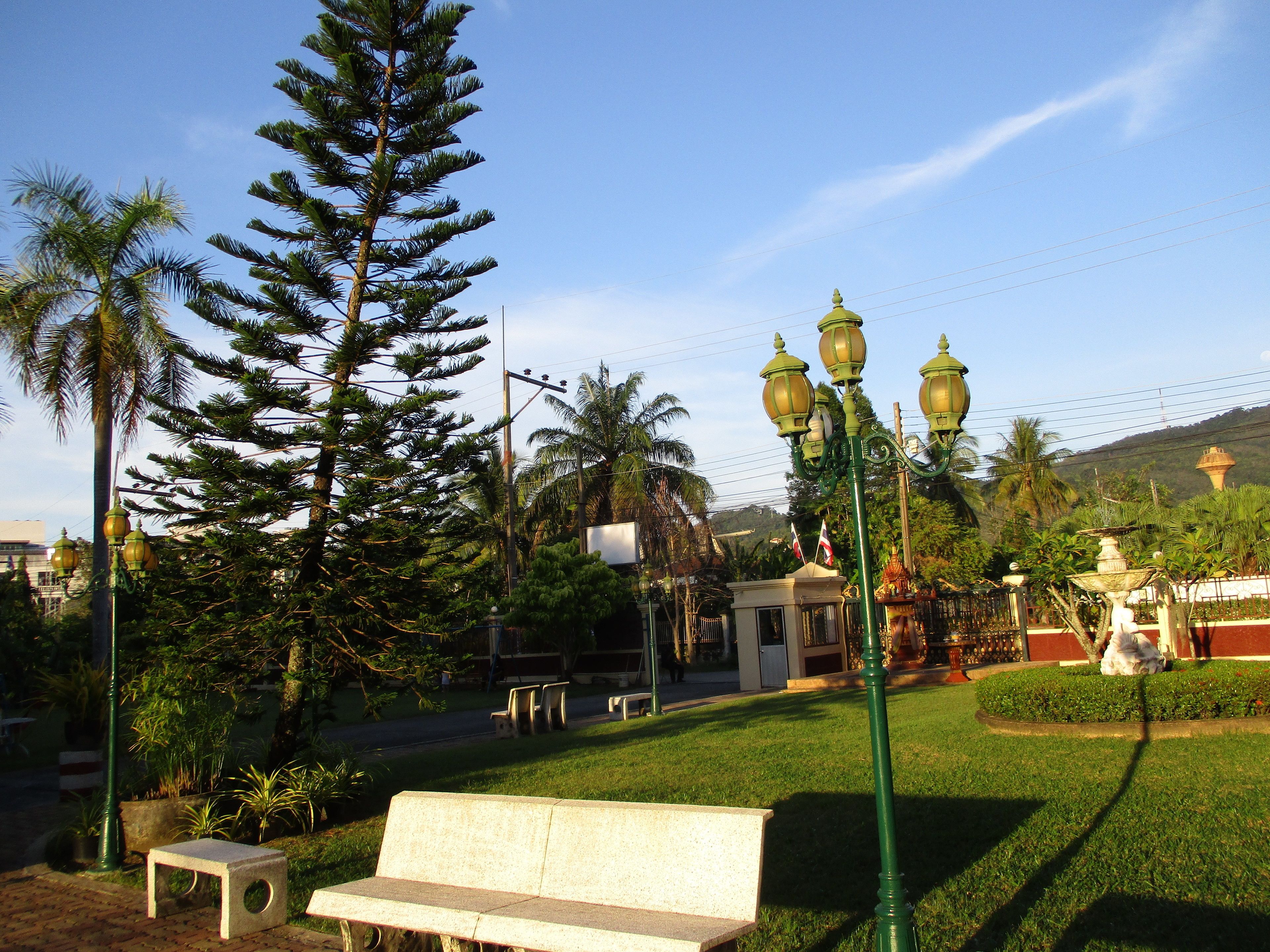 Un parc avec un banc, des lampadaires et une statue.