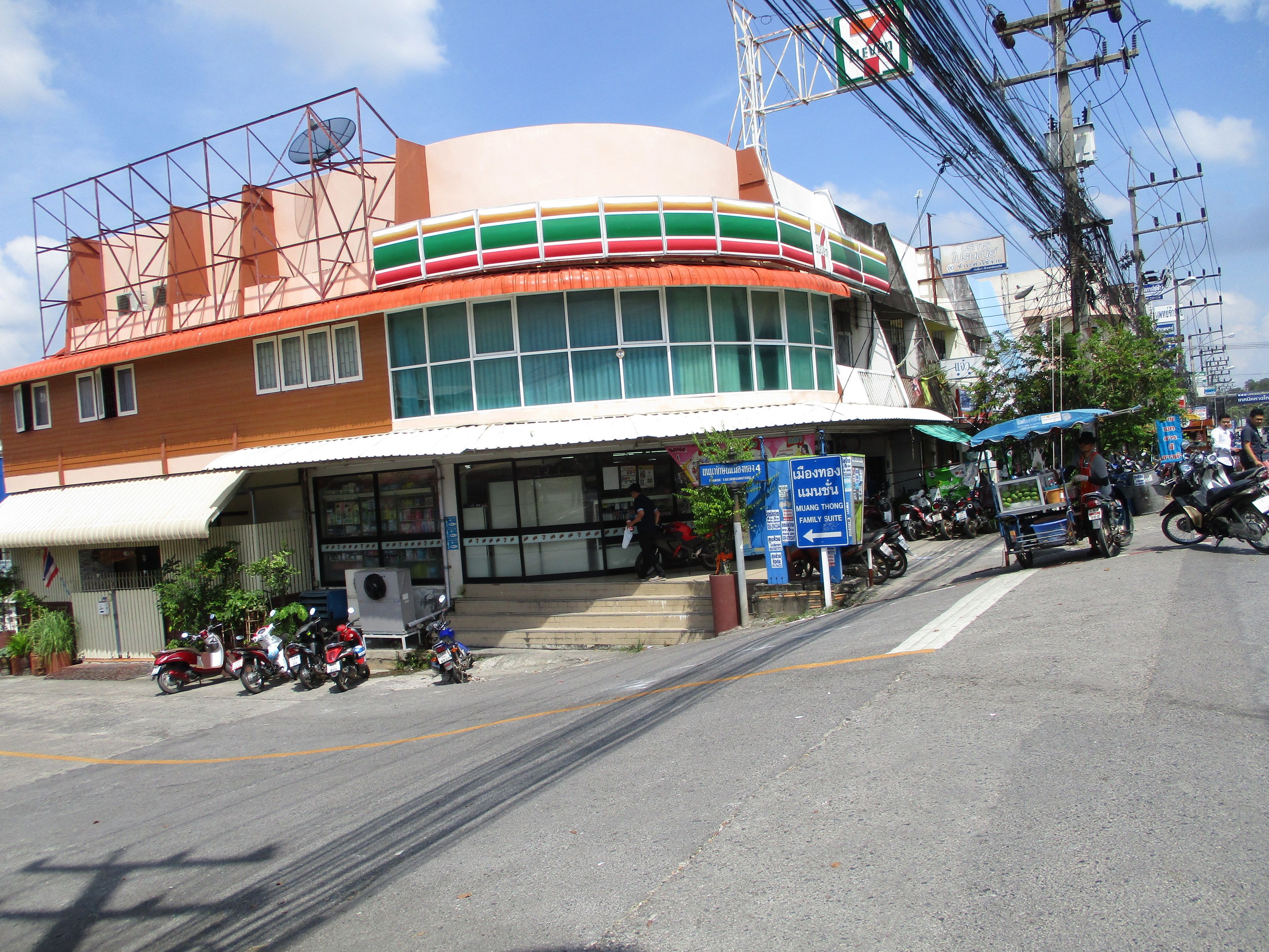 A 7-Eleven store with a large sign, a covered entrance, and a parking area with motorcycles.