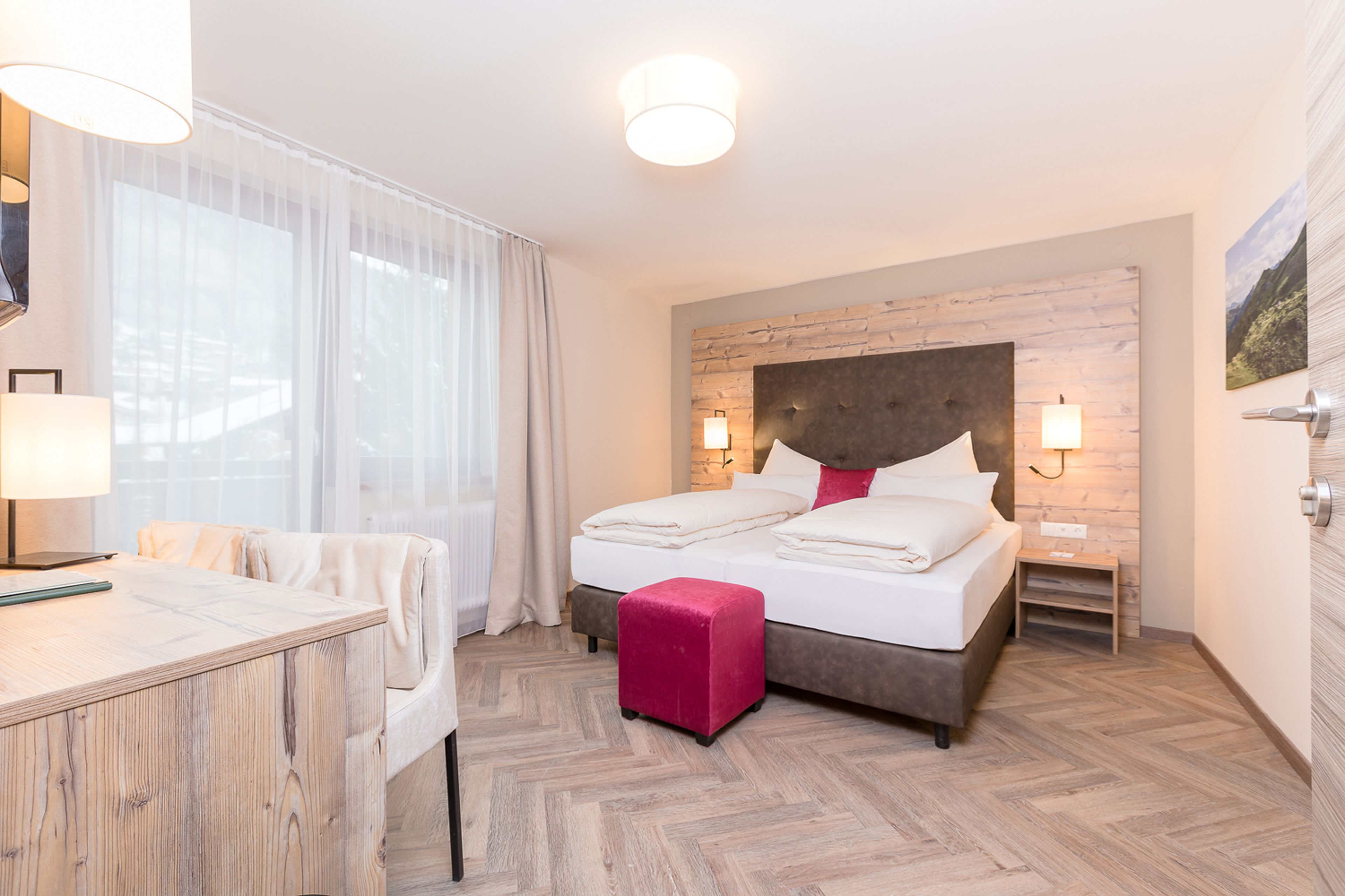 A hotel room with a bed, bedside tables, a desk, and a chair.