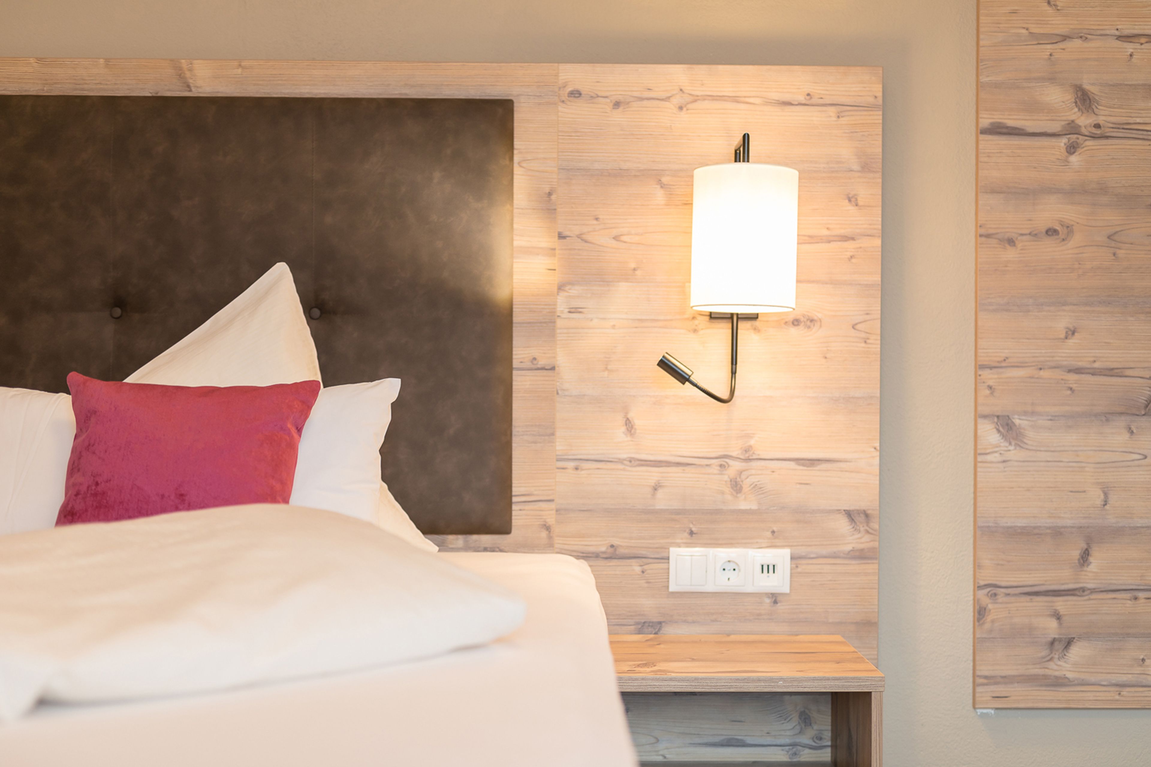A hotel room with a bed, a nightstand, a wall-mounted lamp, and a wooden panel wall.