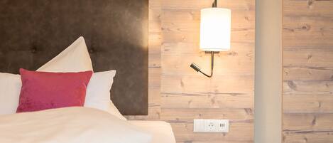 A hotel room with a bed, a nightstand, a wall-mounted lamp, and a wooden panel wall.