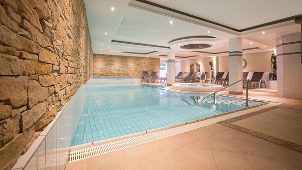 Une piscine intérieure aux murs en pierre, dotée de chaises longues et d’un espace jacuzzi.
