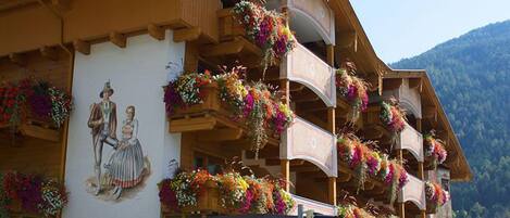 Un hotel con balcones decorados con flores coloridas, un cartel que indica "HOTEL Tirolerhof" y una vista de montañas al fondo.
