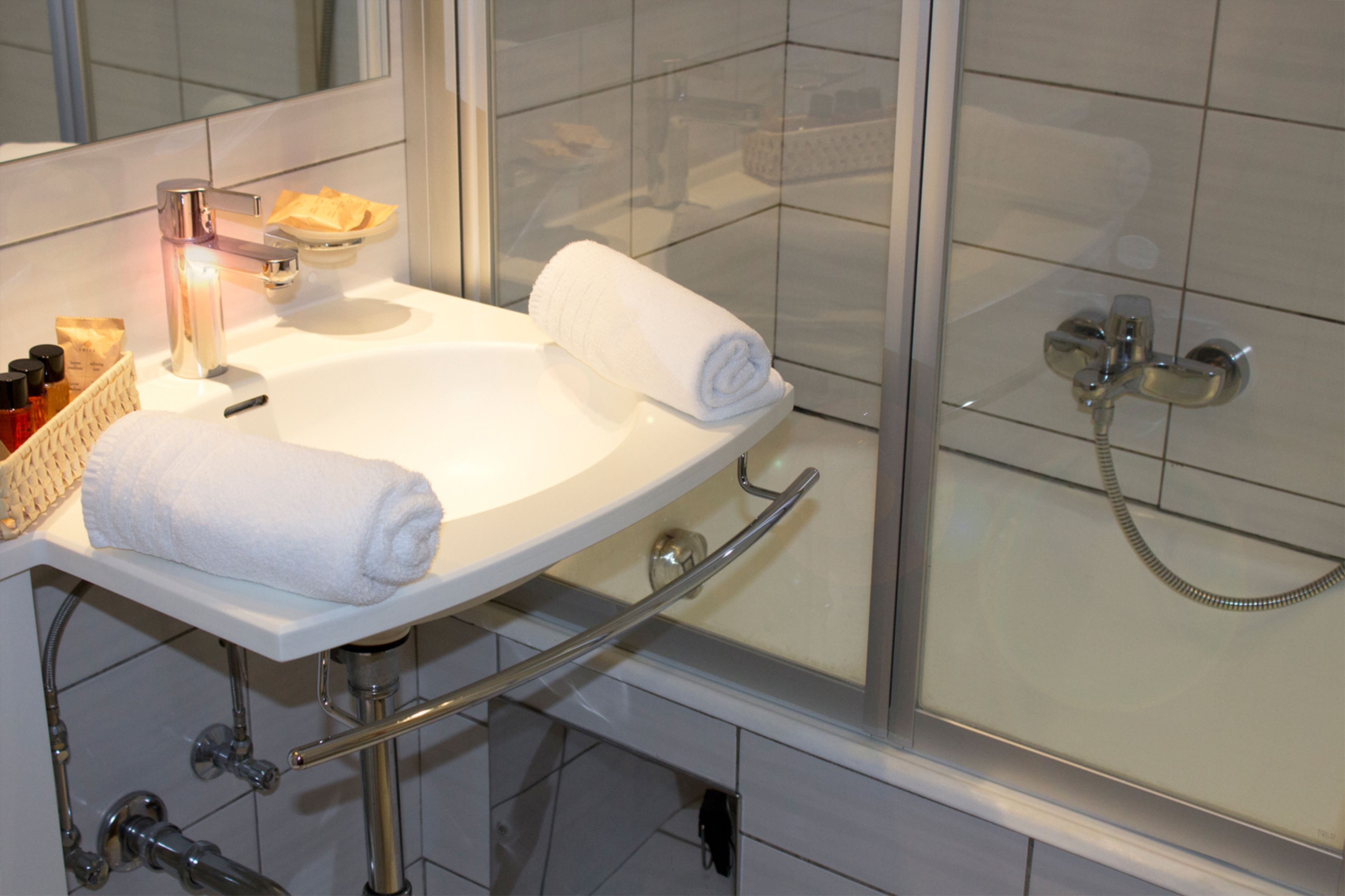 A bathroom with a white sink, two rolled towels, a glass shower enclosure, and a soap dish with bottles.