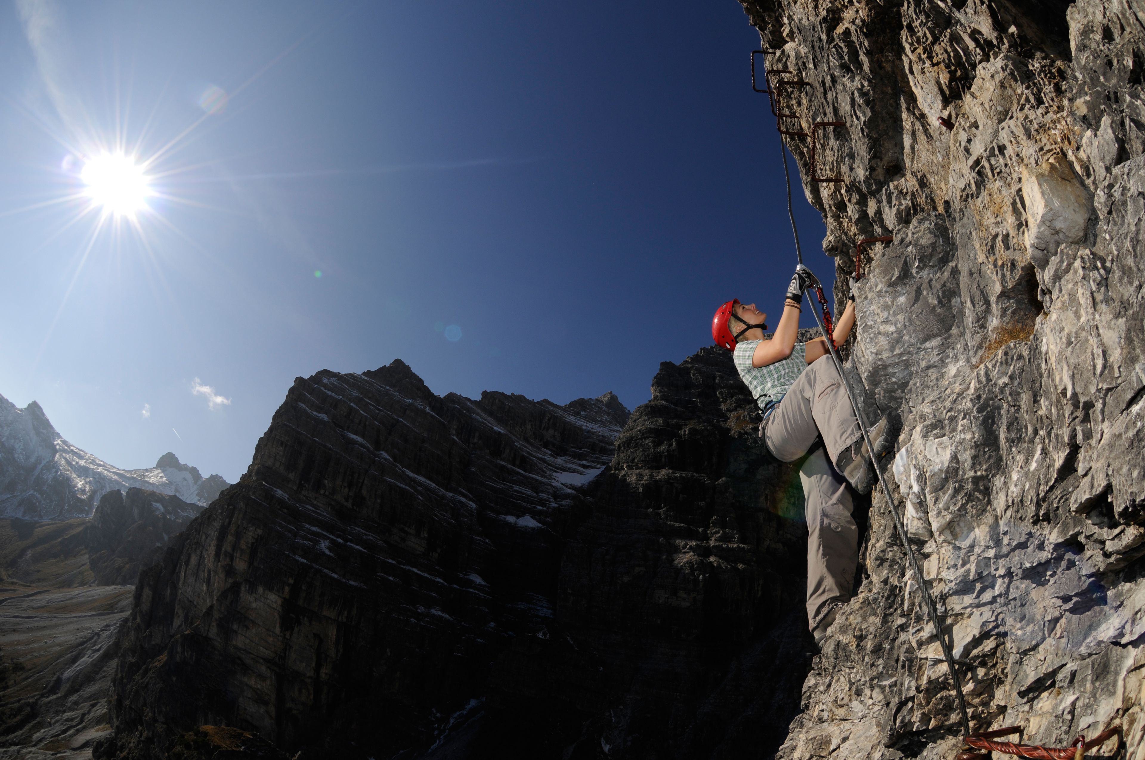 A person climbing a rocky mountain with a clear sky and sun in the background.