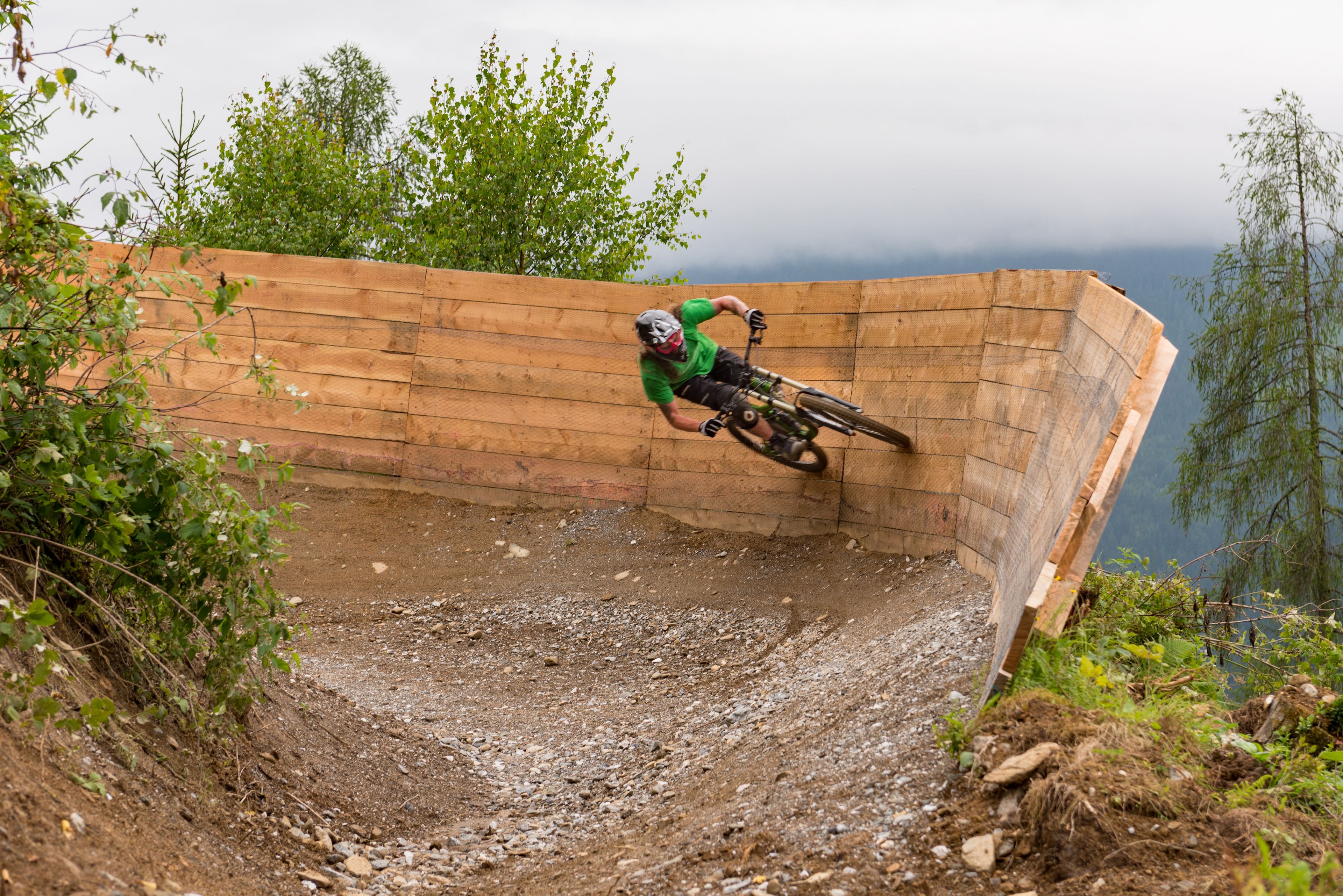 A person riding a mountain bike on a dirt track with a wooden ramp and natural surroundings.